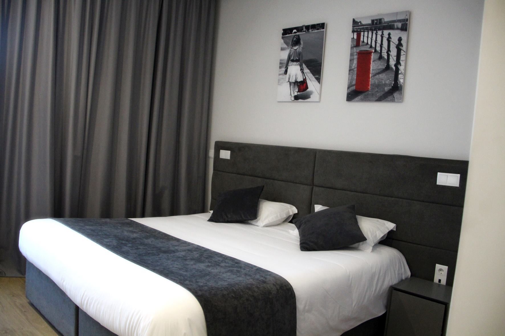 A modern hotel room with a large bed, grey curtains, and two framed pictures on the wall.