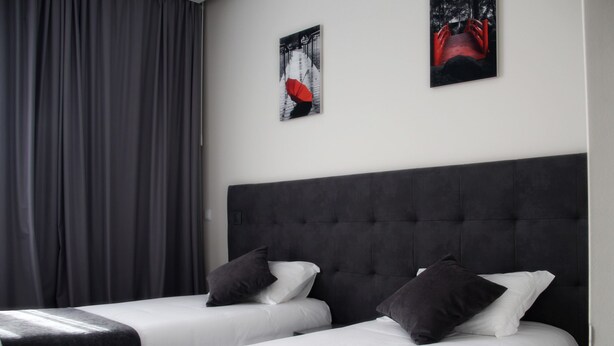 A hotel room with two beds, grey curtains, and two framed pictures on the wall. - Basto Vila Hotel (Cabeceiras de Basto)