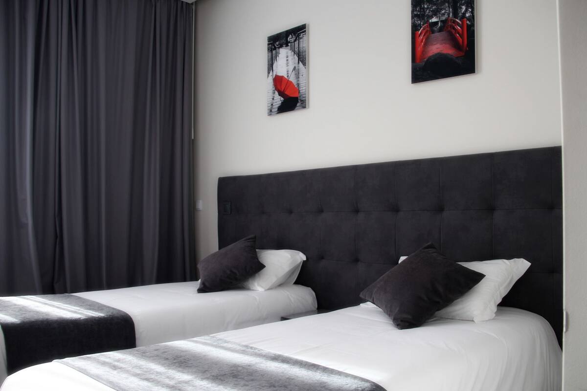 Una habitación de hotel con dos camas, cortinas grises y dos cuadros en la pared.