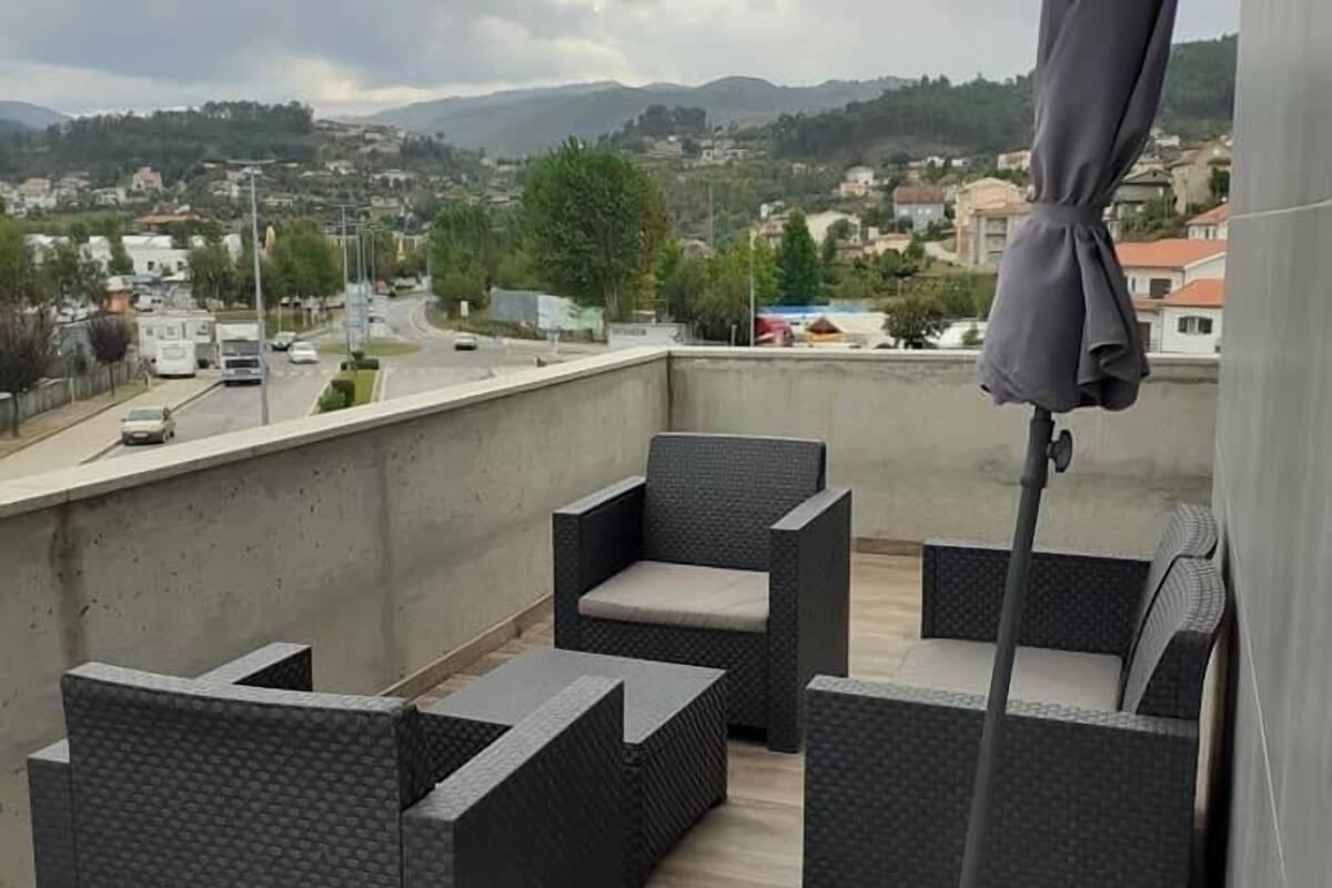Una terraza en la azotea con mobiliario exterior, vistas a un pueblo y un cielo nublado.
