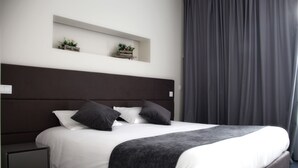 A modern bedroom with a large bed, dark headboard, white bedding, and two small potted plants on a shelf above the bed. - Basto Vila Hotel (Cabeceiras de Basto)