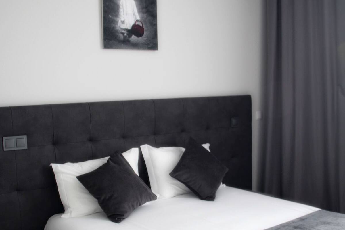 Un dormitorio moderno con una cama grande, una mesita de noche, un control remoto y un cuadro en la pared.