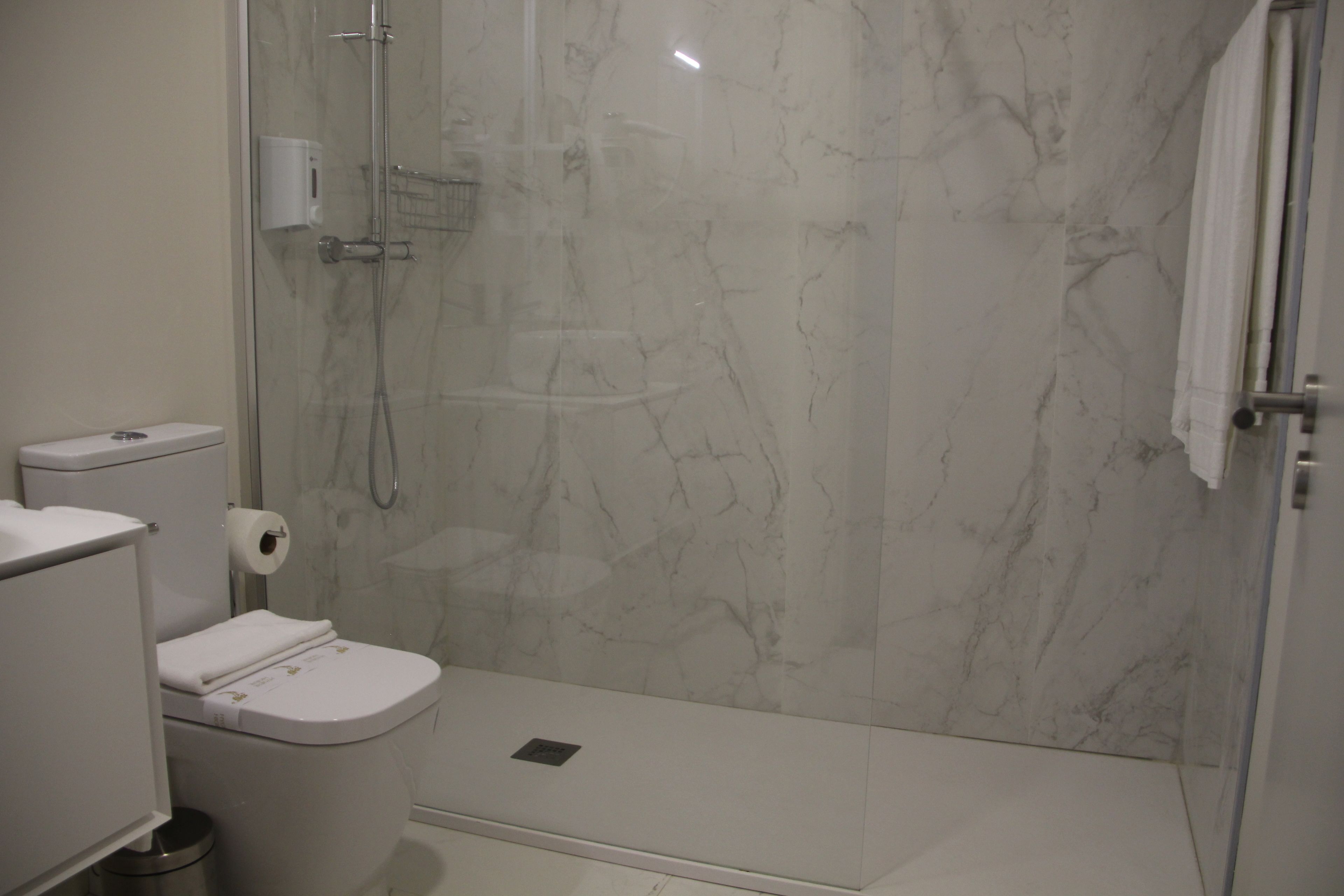 Un baño moderno con ducha de vidrio, inodoro y pared de mármol.