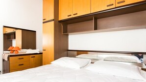 A hotel room with a bed, wooden cabinets, a mirror, and a small table with an orange lamp.