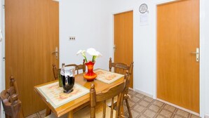 A dining area with a wooden table, chairs, a vase with flowers, a pitcher, and a clock on the wall.