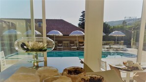 A dining table with a floral centerpiece and dessert glasses, overlooking a pool area with umbrellas and lounge chairs. - Sui Generis (Tropea)