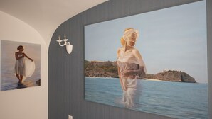 A gallery with two large paintings on the wall, one depicting a person with a surfboard and the other a person by the sea. - Sui Generis (Tropea)