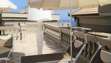 Eine Dachterrasse mit Sitzgelegenheiten im Freien, darunter Tische und Stühle, und großen Sonnenschirmen, die Schatten spenden.