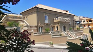 A multi-story building with a symmetrical facade, balconies, and a central entrance with a staircase. - Sui Generis (Tropea)