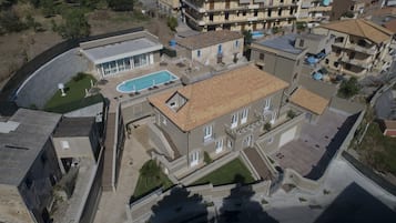 Vue aérienne d’un quartier résidentiel avec une grande maison dotée d’une piscine, de nombreux balcons et d’une entrée sécurisée par un portail.