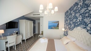 A hotel room with a bed, a desk, a chair, a wardrobe, a painting of a coastal scene, and a chandelier. - Sui Generis (Tropea)