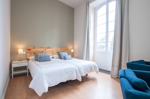 En dobbeltseng med hvide sengetøj, et træhovedgærde, to sengeborde og et natbord med lampe.