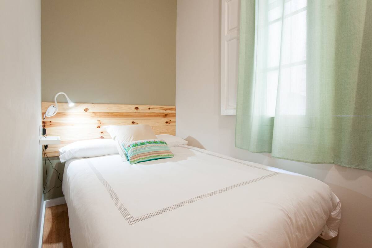 Una cama bien hecha con cabecera de madera, ropa de cama blanca y almohada de estampado verde.