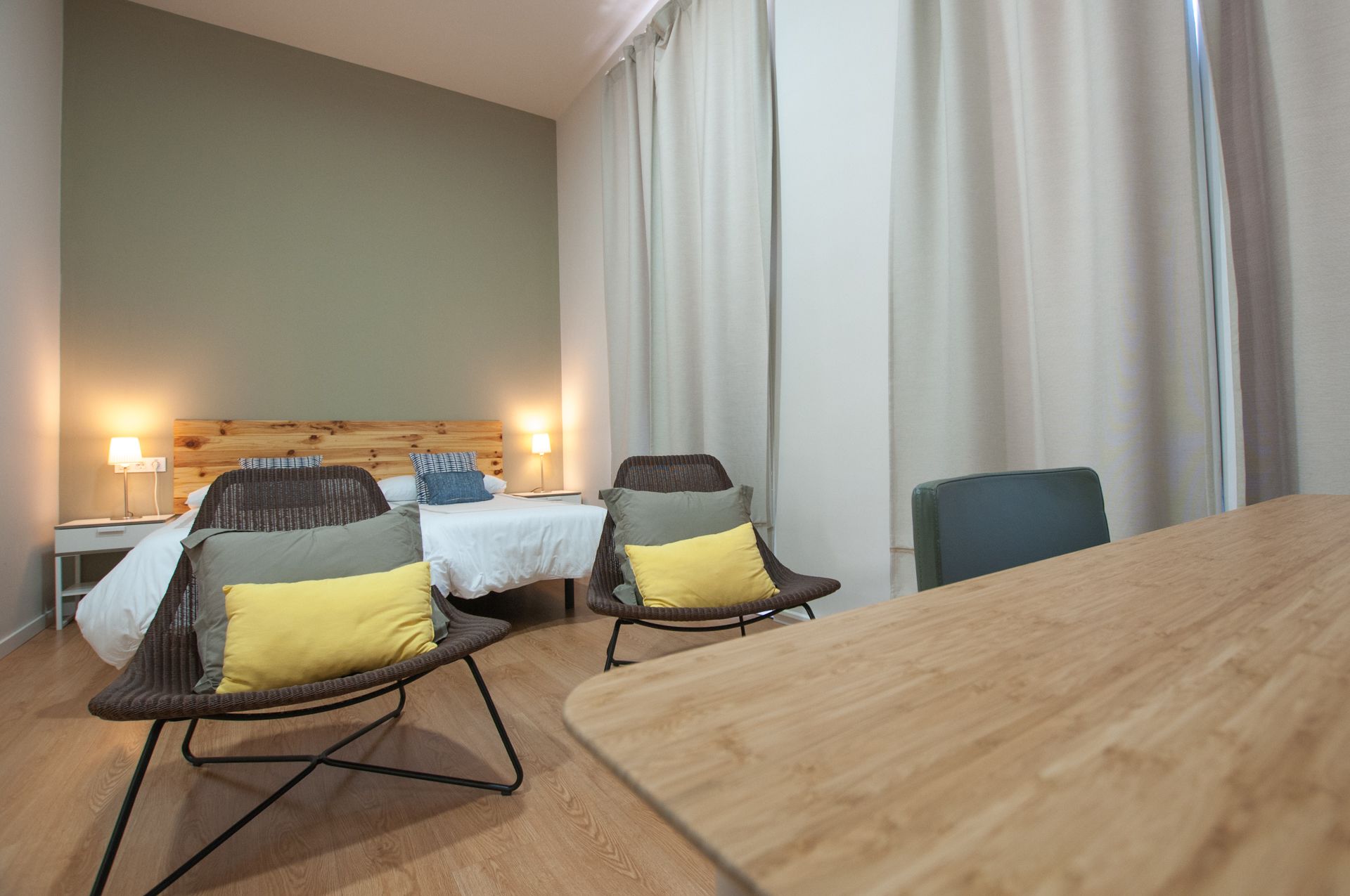 A hotel room with two beds, a wooden table, and two wicker chairs with cushions.