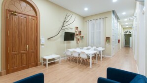 Ein Hotelzimmer mit Holztür, Fernseher, kleinem Tisch und mehreren Stühlen.