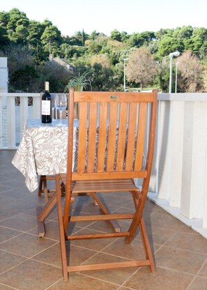 Um conjunto de cadeira e mesa de madeira num pátio ladrilhado, com uma garrafa de vinho e um copo sobre a mesa.