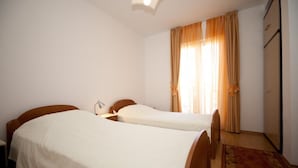 Une chambre avec deux lits simples, une table de chevet avec une lampe, une armoire et une fenêtre avec des rideaux.