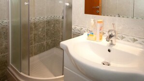 Une salle de bain avec une douche à parois de verre, un lavabo doté d’articles de toilette et un meuble en bois placé au-dessus du miroir.