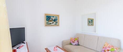 Un soggiorno con un divano, un tavolino da caffè, una televisione e due opere d'arte appese alla parete.