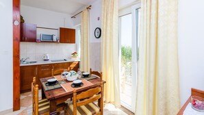 A compact kitchen with wooden cabinets, a microwave, and a dining area with a table set for two. - Apartments Nicol - Two-Bedroom Apartment with Balcony and Sea View (Dubrovnik)