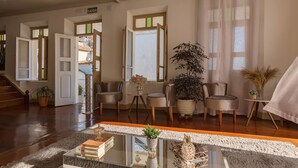 A spacious living area with a wooden floor, a glass coffee table, and several chairs. There are potted plants and a sign that reads "SAÍDA". - Hotel Canto Do Chafariz (Diamantina)