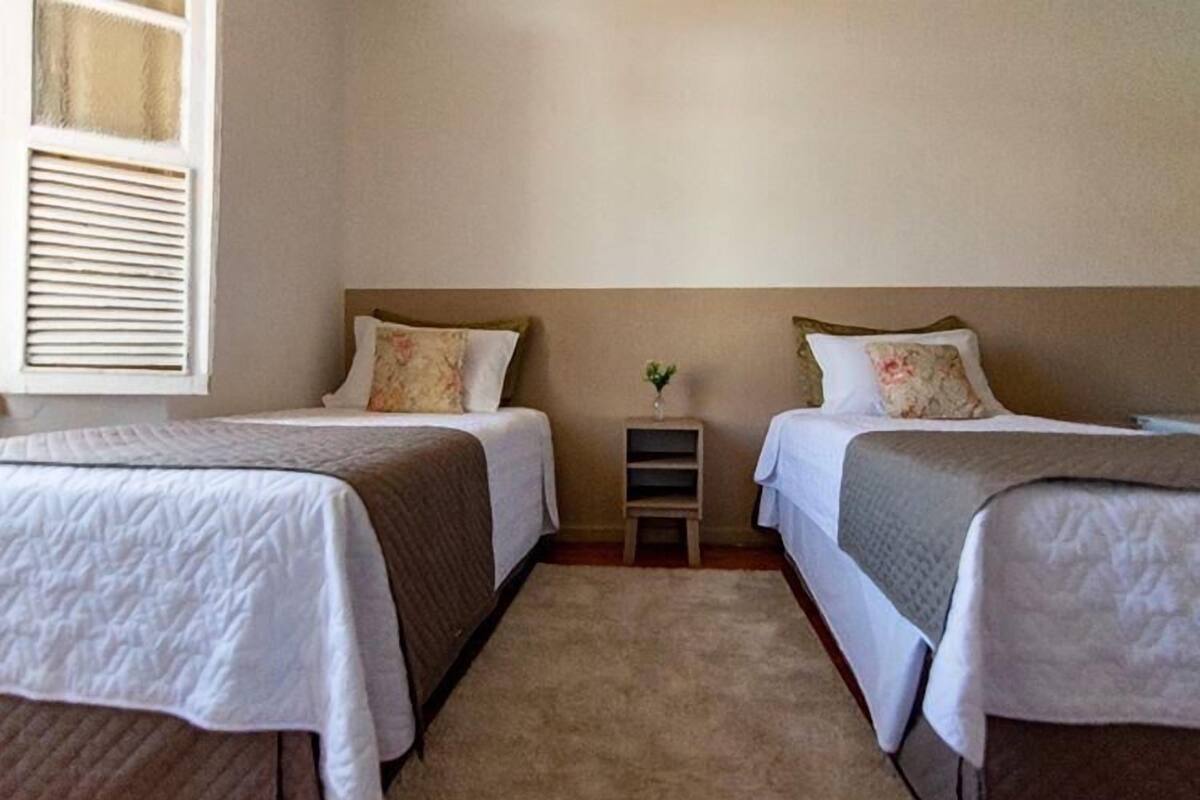 A room with two beds, a small wooden nightstand, and a window with blinds.