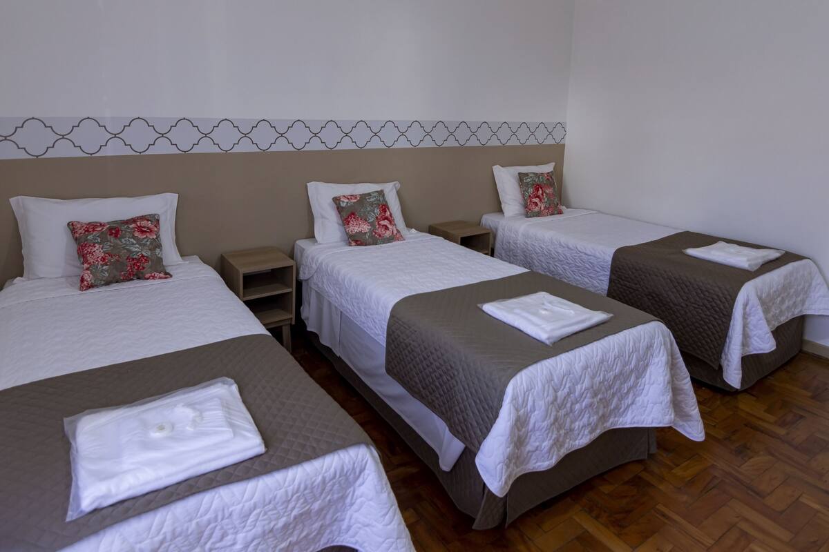 A hotel room with three single beds, each with a pillow and a folded towel.