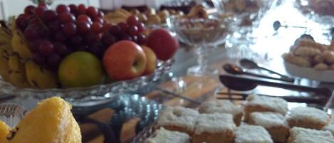 Una mesa con diferentes alimentos, entre ellos frutas, pasteles y postres.