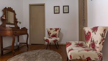 A room with a wooden desk, two chairs with floral upholstery, a round rug, and a door.