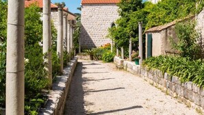 Une ruelle étroite pavée, bordée de bâtiments en pierre et d’une végétation luxuriante.