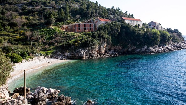 A coastal area with buildings on a hillside, clear turquoise water, and rocky terrain.