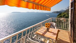 A balcony with a table and chairs, a vase with sunflowers, and a view of the sea and distant mountains.