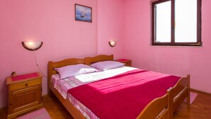 A bedroom with pink walls, a wooden bed, two bedside tables, a window, and a wall-mounted picture.
