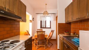 A kitchen with wooden cabinets, a gas stove, a dining table with chairs, and a window with lace curtains.