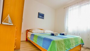 Una cama bien tendida con un colcha colorida, un armario de madera y un pequeño cuadro en la pared.