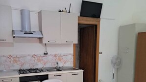 A compact kitchen with a gas stove, a sink, and a microwave. There is a dining table with chairs and a bed with a red blanket.