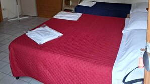 A small, simple room with a bed, a wardrobe, and a fan.