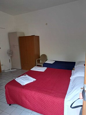 Une petite pièce simple, avec un lit, une armoire et un ventilateur.