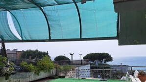 An outdoor patio with a table and chairs, a green artificial lawn, and a view of the sea.