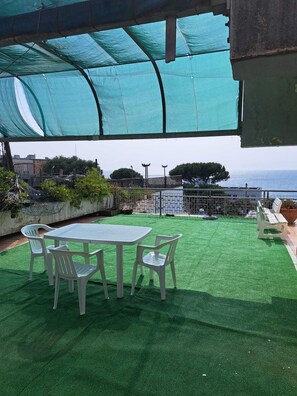 Une terrasse extérieure avec une table et des chaises, une pelouse artificielle verte et une vue sur la mer.