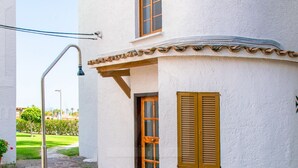 Eine weiße Villa mit gefliestem Patio, einem Metallgeländer und einer Holztür.