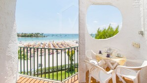 Ein Balkon mit Blick auf Strand und Meer, ein Tisch mit Stühlen und ein kleines Fenster.