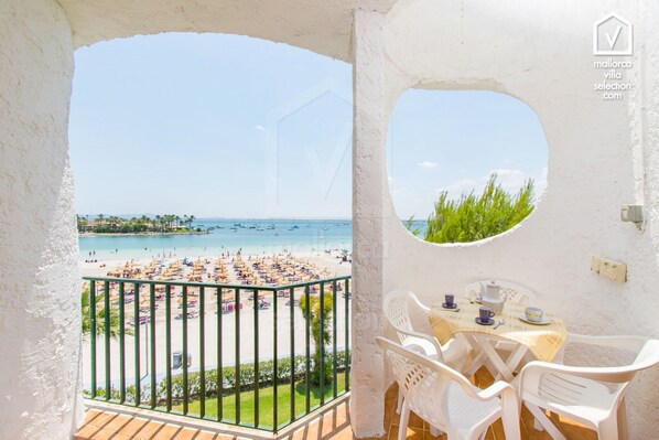 Un balcon donnant sur une plage et la mer, une table avec des chaises et une petite fenêtre.