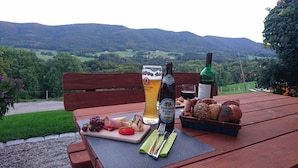 A wooden table with a meal, a beer bottle, and a glass of beer. - Spacious Schneiderhof vacation apartment with terrace (Neukirchen)
