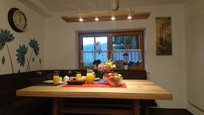 A dining area with a wooden table set for breakfast, a window with curtains, and a clock on the wall. - Spacious Schneiderhof vacation apartment with terrace (Neukirchen)