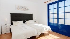 A bedroom with a double bed, two bedside tables, a nightstand, a blue door, and a wall-mounted artwork. - Spacious Apartment "Casa Nancy" with Mountain View, Pool, Wi-Fi & Terrace (Yaiza)