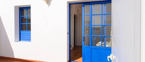 A white building with a blue door and window, a tiled floor, and a small wall-mounted light fixture.