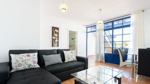 A modern living room with a black sofa, glass coffee table, and a view through a large window. - Spacious Apartment "Casa Nancy" with Mountain View, Pool, Wi-Fi & Terrace (Yaiza)
