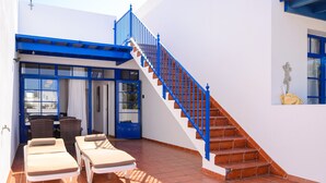 A covered outdoor area with a staircase, lounge chairs, and a dining table. - Spacious Apartment "Casa Nancy" with Mountain View, Pool, Wi-Fi & Terrace (Yaiza)