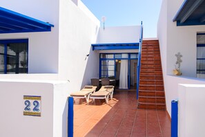 A narrow courtyard with a staircase, a seating area with chairs and a table, and a number '22' sign on the wall.